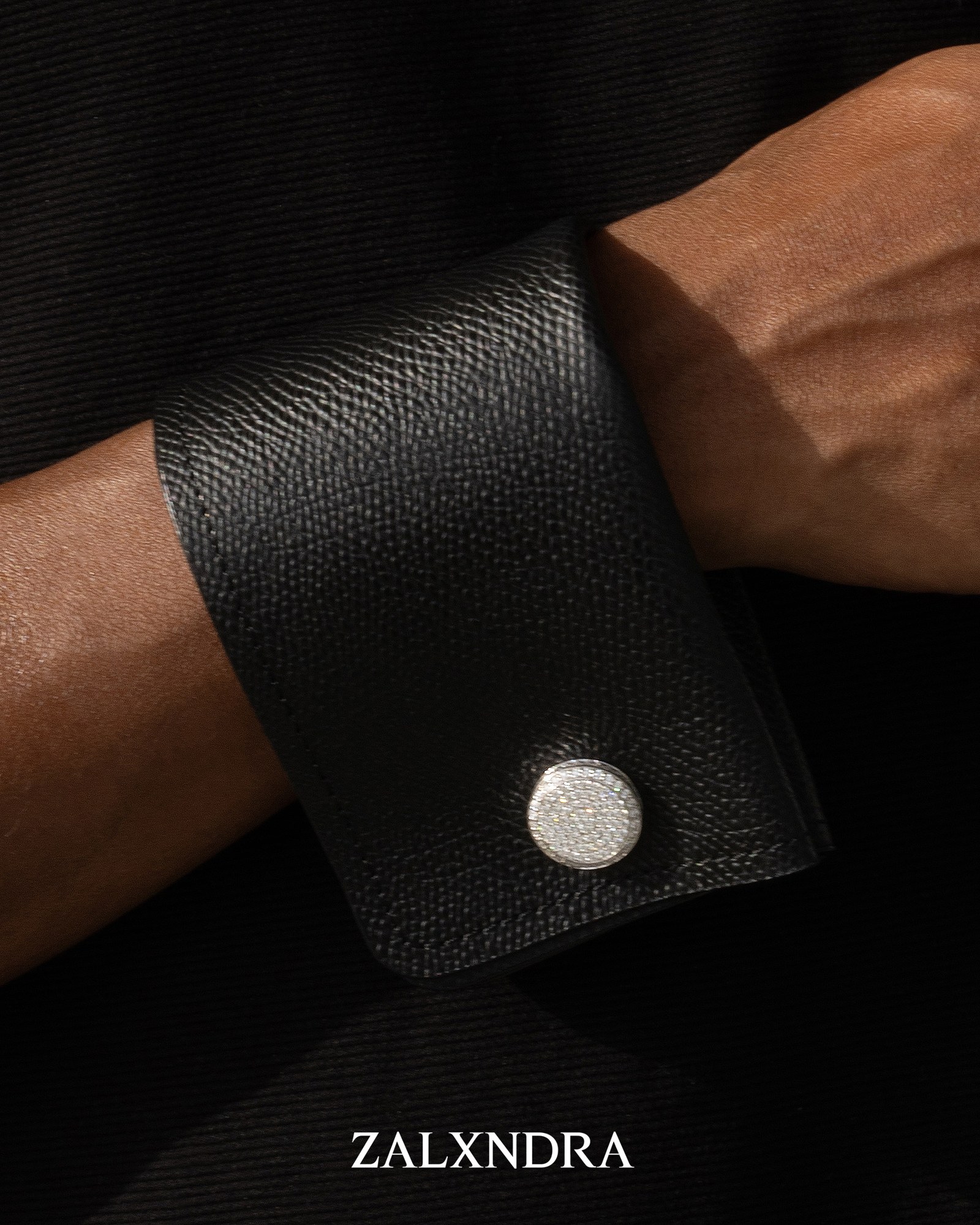 Close-up of the circular cufflink against black grained leather
